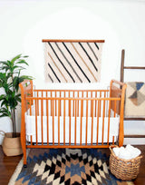 Cozy nursery with a wooden crib, white bedding, plant, blanket ladder, and eco-friendly decor featuring a Handmade in Ukraine Organic 100% Sheep Wool Woven Rug Wall Hanging.