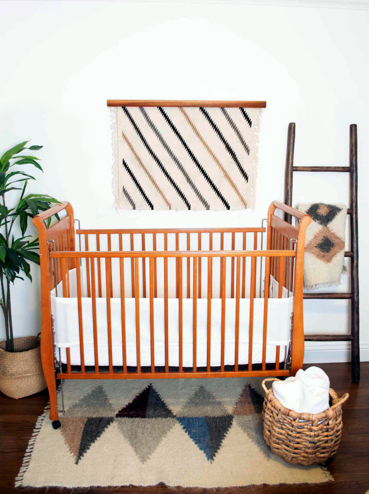 A nursery features a wooden crib, a plant, and a woven basket, with the standout eco-friendly decor: the Handmade in Ukraine Organic 100% Sheep Wool Woven Rug Wall Hanging.
