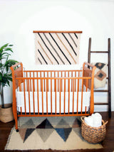 A nursery features a wooden crib, a plant, and a woven basket, with the standout eco-friendly decor: the Handmade in Ukraine Organic 100% Sheep Wool Woven Rug Wall Hanging.