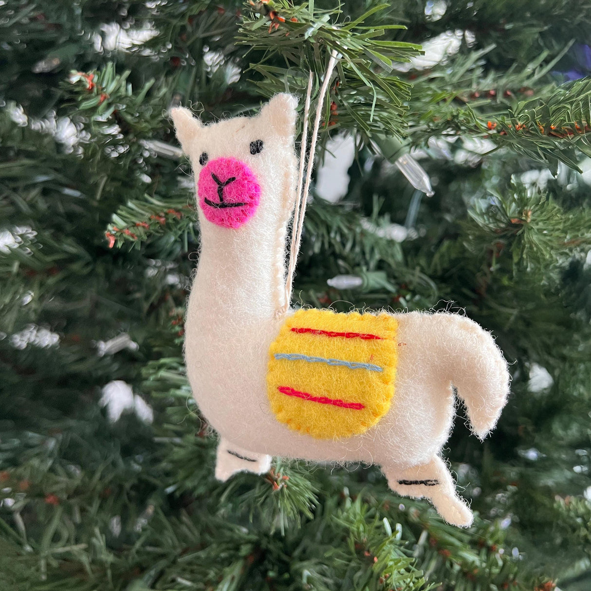 The Hand-Stitched Felted Llama Ornament features a yellow saddle and hangs on your Christmas tree, adding a cheerful touch to your holiday decor.