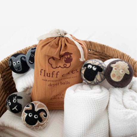 A basket with rolled white towels and a brown Fluff Ewes bag displays the Gift Bundle: Buy 3 Sets of Fluff Ewes Natural Dryer Balls, Get 1 Set Free—each set includes six eco-friendly organic wool dryer balls made from New Zealand wool.