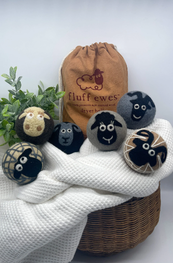 The Gift Bundle: Buy 3 Sets of Fluff Ewes Natural Dryer Balls, Get 1 Set Free! includes eco-friendly wool dryer balls on a wicker basket with a brown Fluff Ewes bag and a white towel.